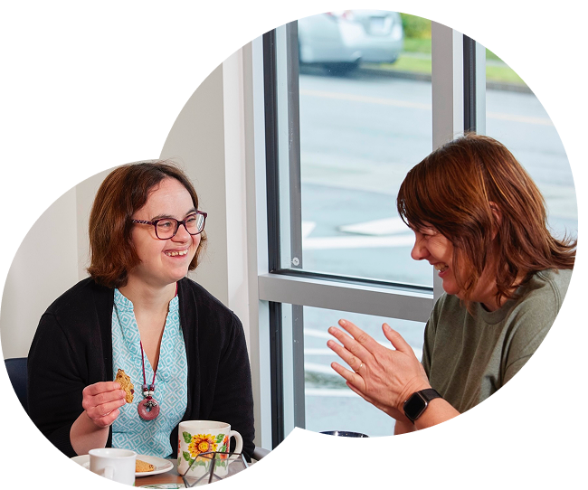 home-hero-smiles Two women laughing and smiling at each other, sitting at a table enjoying some tea